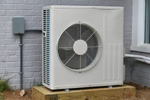Single white HVAC condenser unit on timber base against grey brick exterior wall