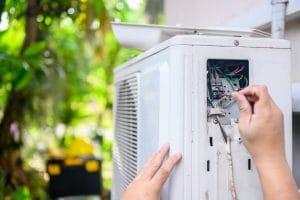 Technician repairing open electrical panel on outdoor air conditioning unit in garden